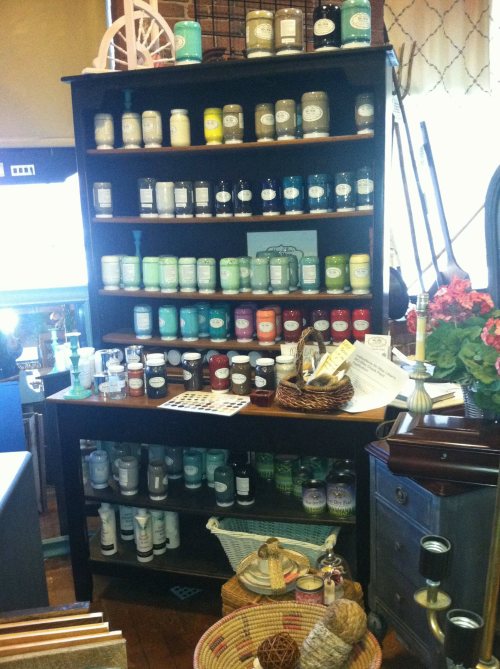 A wooden display shelf filled with various colorful candles and decorative items in a cozy shop setting.