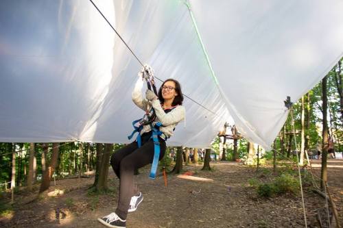 A person in a harness zip-lining through a forested area, smiling and enjoying the outdoor adventure.
