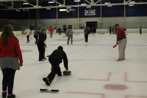 A group of people curling on an ice rink, with some participants sliding stones and others observing.