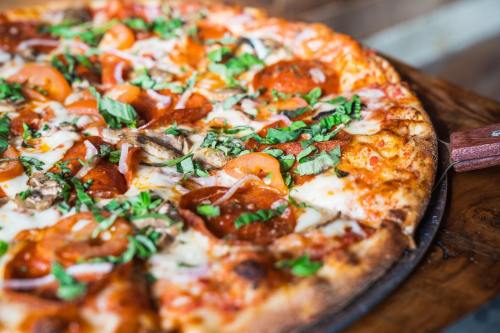Close-up of a delicious pizza topped with pepperoni, mushrooms, tomatoes, and fresh basil on a wooden table.