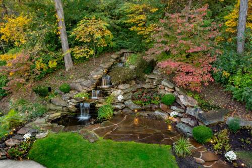 A serene garden with a cascading waterfall, surrounded by colorful autumn foliage and neatly arranged plants.