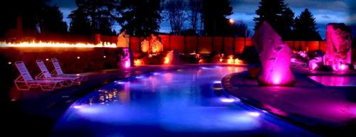 A beautifully lit pool area at night, featuring colorful lights, lounge chairs, and a serene atmosphere.