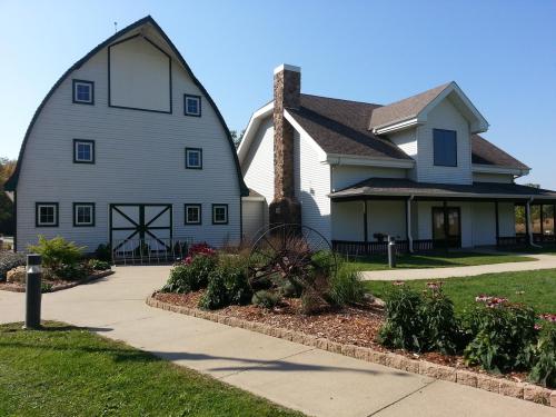 A white barn with a unique roof design next to a modern house, surrounded by a landscaped garden and pathway.