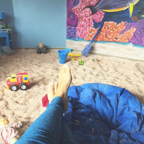 A child's play area with a blue bean bag, toys, and a colorful coral mural on the wall. Feet are visible in the foreground.