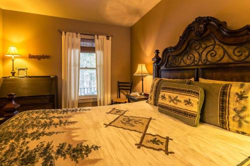 Cozy bedroom with a wooden bed, decorative pillows, warm lighting, and a window with sheer curtains.