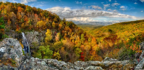 A panoramic view of a vibrant autumn landscape with colorful trees and a waterfall cascading down rocky cliffs.