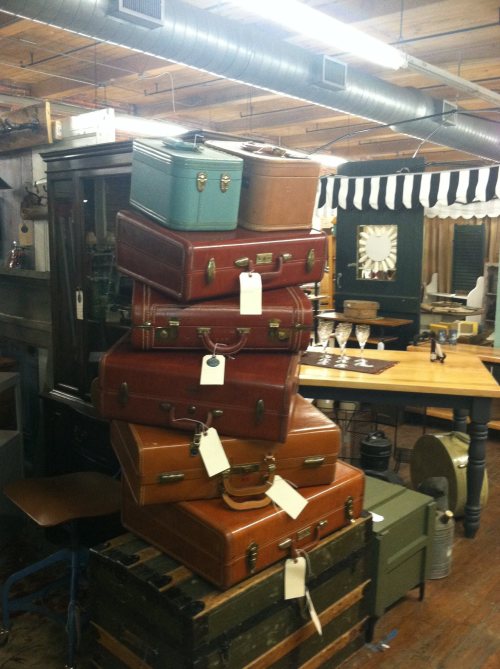 A stack of vintage suitcases in various colors and sizes, displayed in a rustic shop setting.