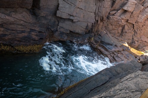 Waves crashing against rocky cliffs, creating foam in a secluded coastal pool.