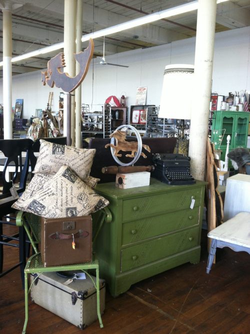 A vintage furniture display featuring a green dresser, a typewriter, decorative pillows, and various eclectic items.