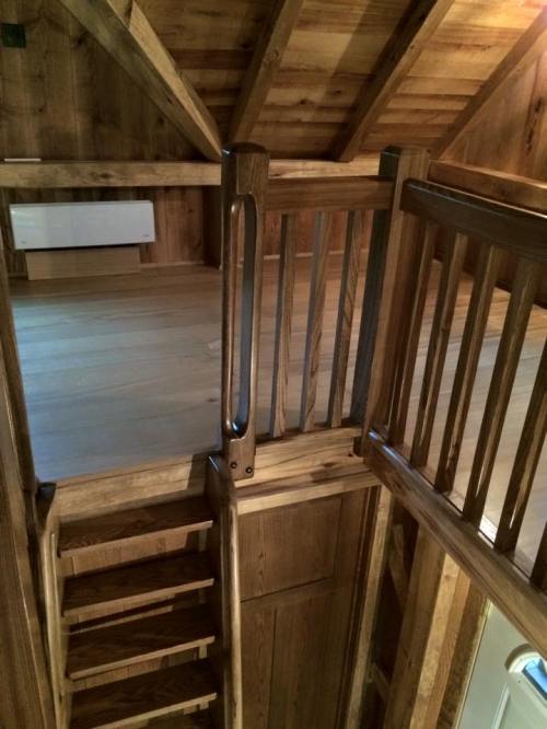 Wooden staircase leading to a loft area, featuring rustic railings and a warm, cozy interior.
