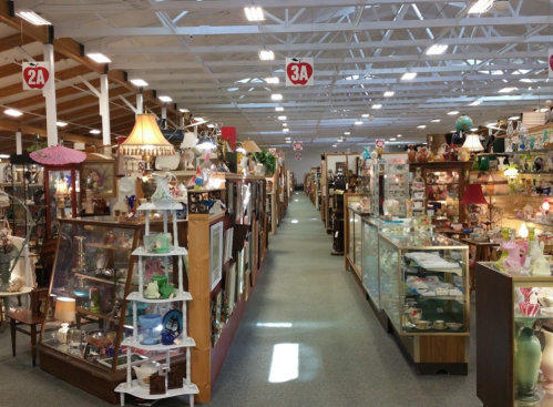 A spacious antique shop aisle lined with display cases and various vintage items, including lamps and collectibles.