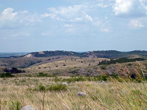 A scenic view of rolling hills and grassy plains under a partly cloudy sky.