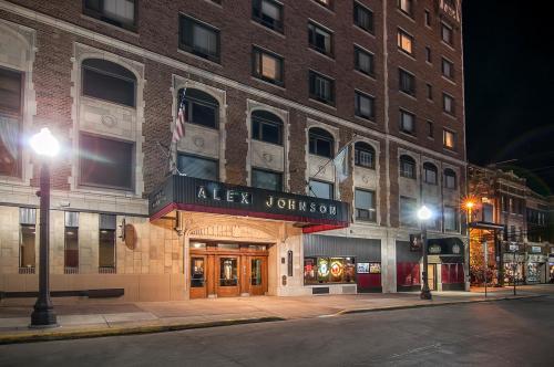 The historic Alex Johnson Hotel entrance at night, featuring brick architecture and illuminated signage.