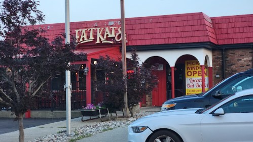 Exterior of Fat Kats restaurant with a red roof, open sign, and parked cars in front.