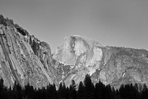 Black and white image of a mountain peak surrounded by trees, showcasing rugged cliffs and a clear sky.