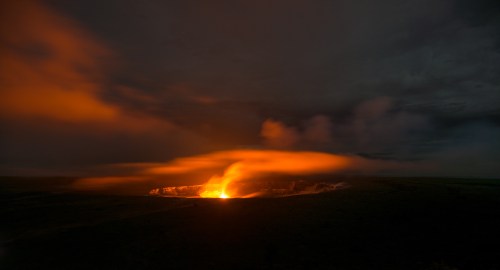 A glowing volcano erupts at night, with orange lava and smoke contrasting against a dark sky.