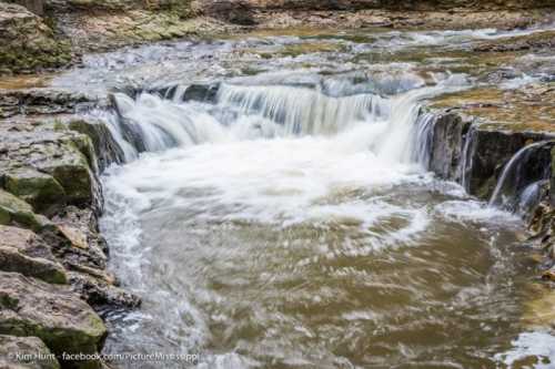 A serene waterfall cascades over rocky terrain, creating a gentle flow of water in a natural setting.