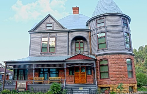 Victorian-style house with a turret, intricate detailing, and a porch surrounded by greenery.