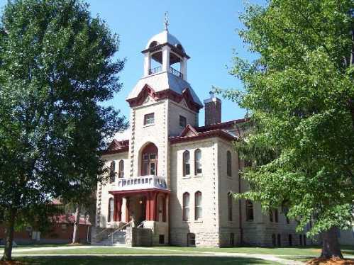 Historic building with a clock tower, surrounded by trees and a clear blue sky.