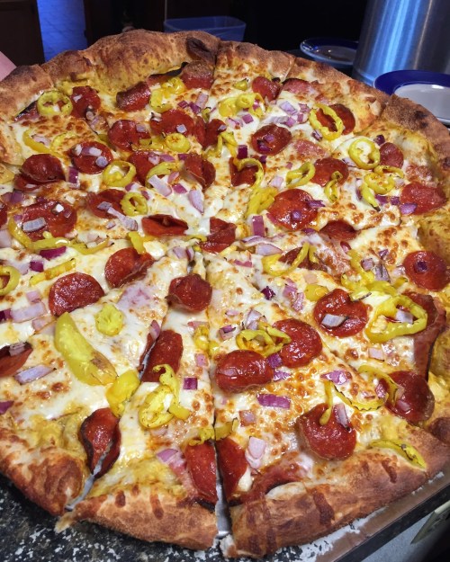 A large pizza topped with pepperoni, yellow peppers, onions, and cheese, sliced into triangular pieces.