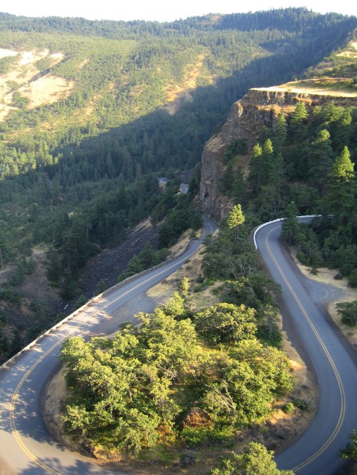 Winding road through lush green mountains, with steep cliffs and trees lining the route.