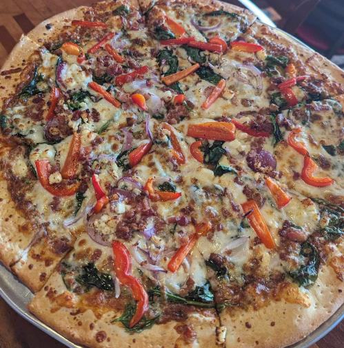 A freshly baked pizza topped with spinach, red peppers, onions, and cheese, served on a round metal tray.