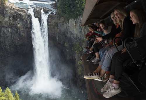 A group of people joyfully sitting on a ledge overlooking a stunning waterfall.