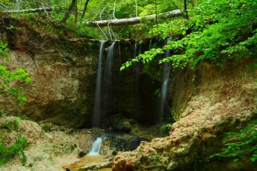 A serene waterfall cascades over rocky terrain, surrounded by lush green foliage in a tranquil forest setting.