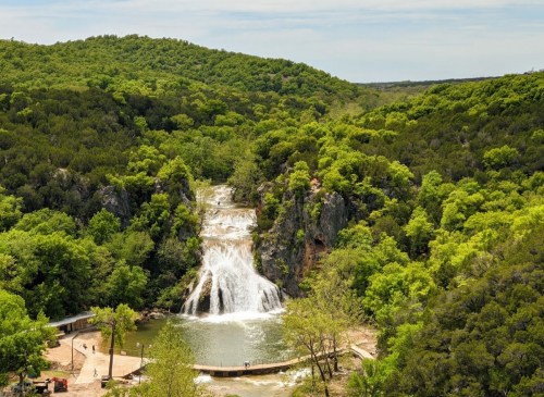 A scenic view of a waterfall cascading into a serene pool, surrounded by lush green trees and hills.