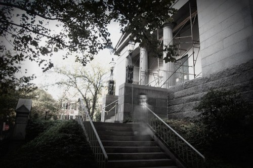 A ghostly figure descends stone steps outside a historic building, surrounded by trees and scaffolding.