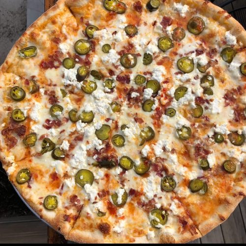 A large pizza topped with jalapeños, crumbled cheese, and a golden crust, served on a wooden surface.