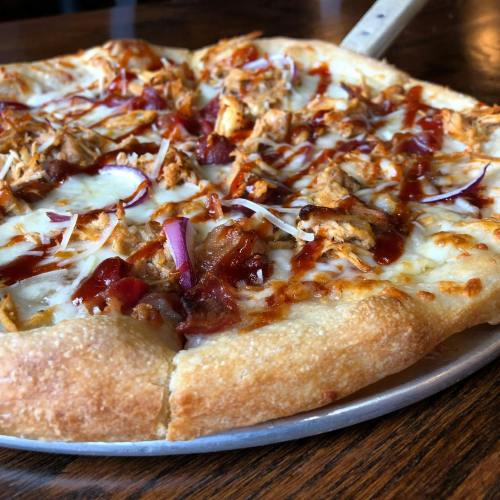 A close-up of a BBQ chicken pizza with cheese, red onions, and a golden crust on a metal pizza pan.