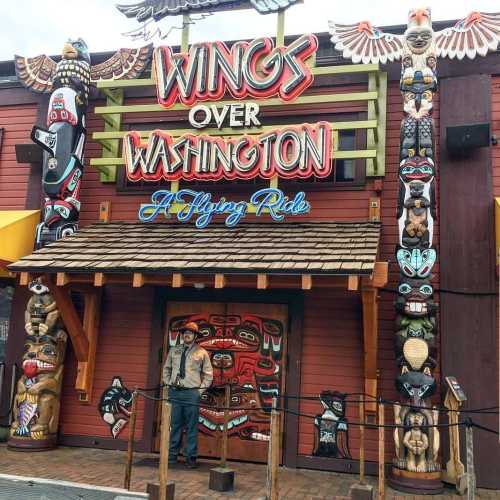 Colorful entrance to "Wings Over Washington" featuring totem poles and a sign for a flying ride attraction.