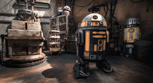 A detailed scene featuring various droids in a workshop, with a prominent blue and orange droid in the foreground.