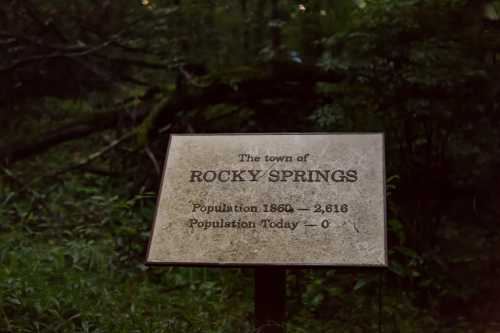 Sign for Rocky Springs, showing a population of 2,616 in 1860 and 0 today, surrounded by dense greenery.