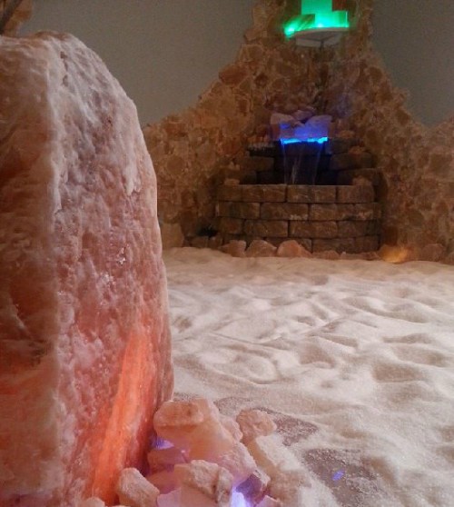 A tranquil salt room with a stone wall, a water feature, and soft lighting, creating a serene atmosphere.