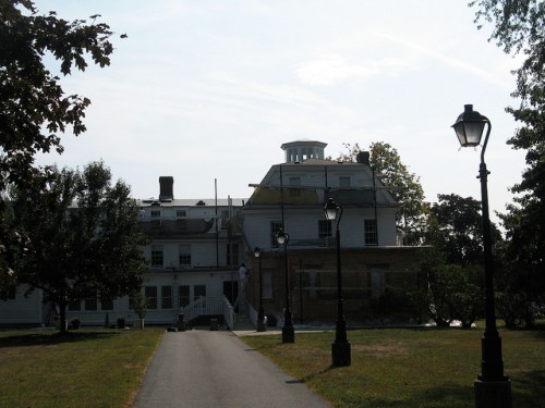 A large, historic building with a cupola, surrounded by trees and street lamps, set against a clear sky.