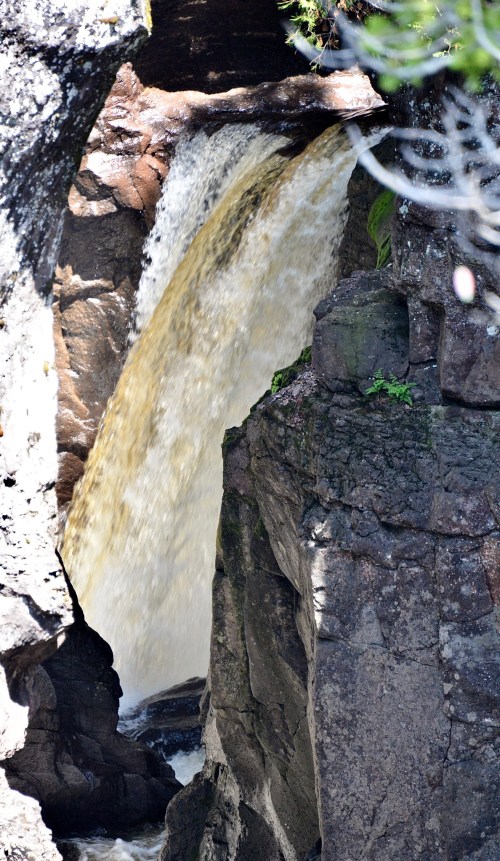 A waterfall cascading down rocky cliffs, surrounded by greenery and natural textures.