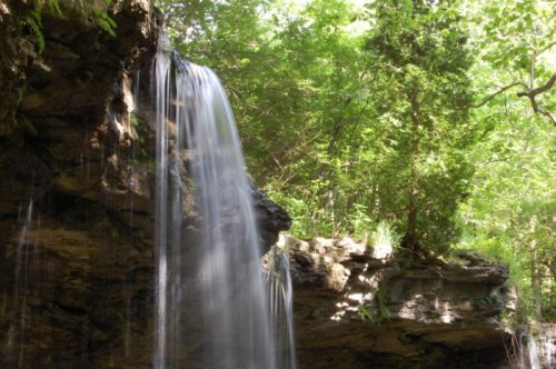 A serene waterfall cascading over rocky cliffs, surrounded by lush green trees and foliage.