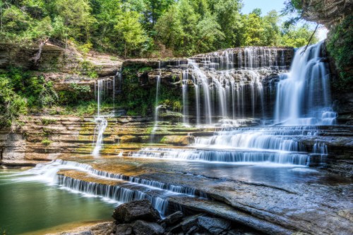 A picturesque waterfall cascading over rocky ledges into a serene pool, surrounded by lush greenery.