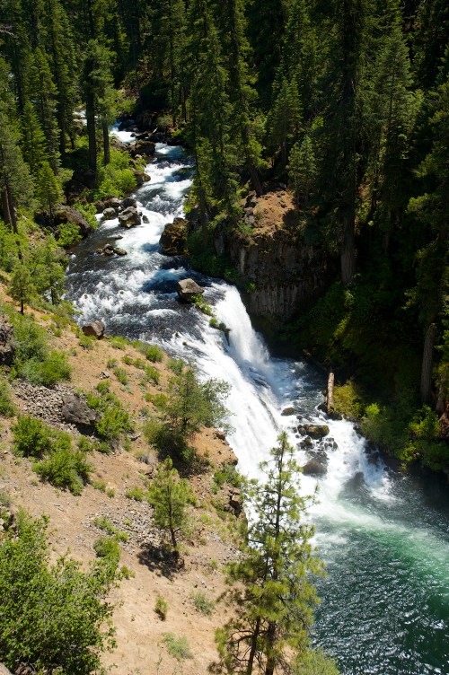 A scenic view of a river cascading through a forested landscape, surrounded by lush greenery and rocky terrain.