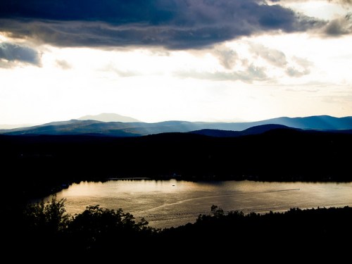 A serene lake reflects the sky, surrounded by mountains under a cloudy sunset.