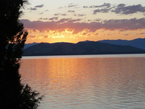 Sunset over a calm lake, with mountains in the background and colorful clouds reflecting on the water's surface.