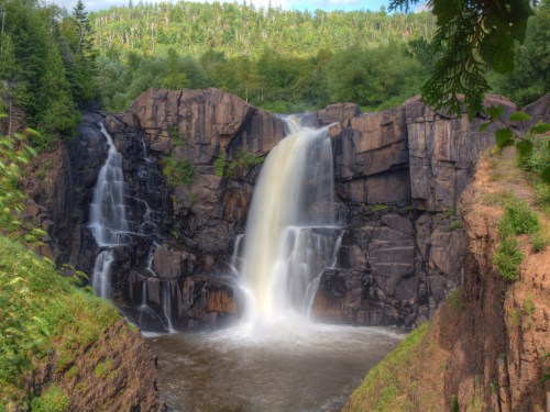 A scenic waterfall cascading over rocky cliffs, surrounded by lush greenery and a tranquil river below.