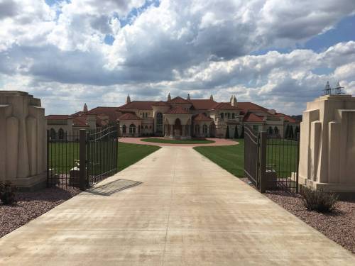 A grand mansion with a red-tiled roof, framed by gates and a wide pathway, under a cloudy sky.