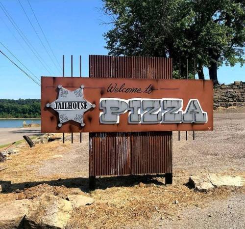Sign reading "Welcome to Jailhouse Pizza" with a sheriff's star, set against a rustic background.
