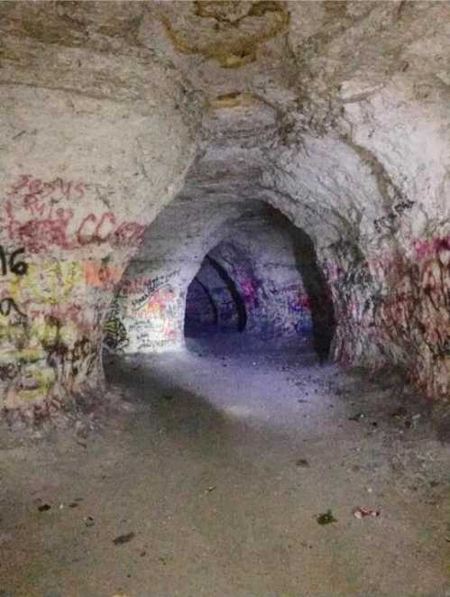 A dimly lit cave tunnel with graffiti on the walls and a sandy floor, creating an eerie atmosphere.