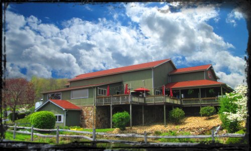A large, two-story building with a red roof, surrounded by greenery and a blue sky with fluffy clouds.
