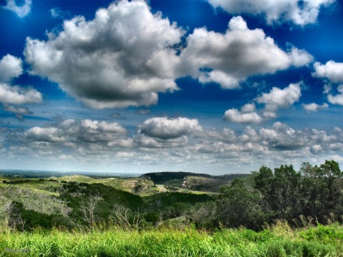 A scenic landscape featuring rolling hills, lush greenery, and a dramatic sky filled with fluffy clouds.