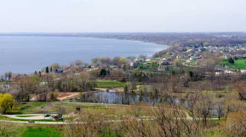 Aerial view of a serene lake surrounded by trees, parks, and residential areas on a clear day.